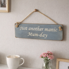 Load image into Gallery viewer, Decorative sign with 'Just another manic Mum-day' text hanging on a wall with a cup and flowers below.