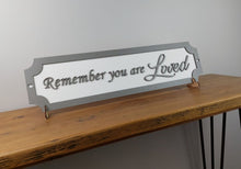 Load image into Gallery viewer, A 3D wooden sign with the phrase 'Remember you are loved' displayed on a table.